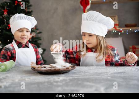 Kinder kochen WeihnachtsLebkuchen. Bruder und Schwester schmücken die Kekse mit Puderzucker zu Hause. baker girl. Hausgemachte Kuchen zu Weihnachten Stockfoto