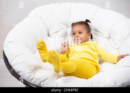 Kleine afroamerikanische Mädchen verwöhnt und spielt in einem Sessel. Stockfoto