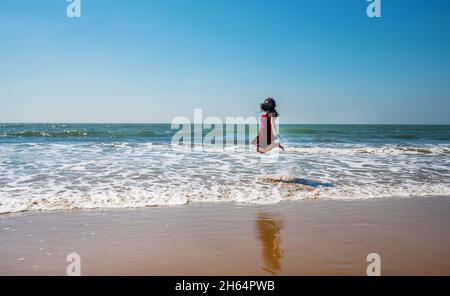 Eine junge Inderin springt fröhlich auf einen paradiesischen Strand in Goa (unkenntlich, weil ihr Haar ihr Gesicht bedeckt) Stockfoto