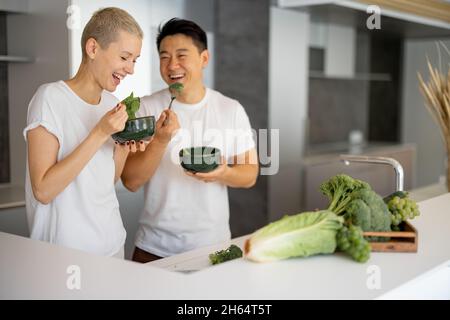 Lachende Pärchen essen Salat in der Küche zu Hause Stockfoto
