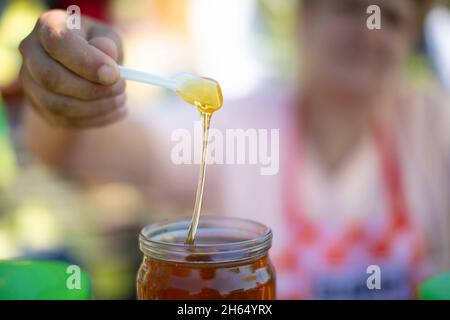 Die Hand eines Imkers gießt Honig aus einem Glas mit einem Löffel. Stockfoto