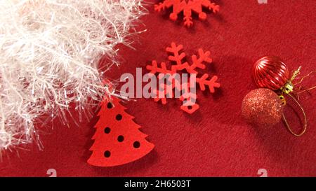 Weihnachtsdekoration: Rote Weihnachtsdekorationen aus Filz in Form eines Weihnachtsbaums schnallen Schneeflocken vor einem roten Hintergrund mit weiß glänzend Stockfoto