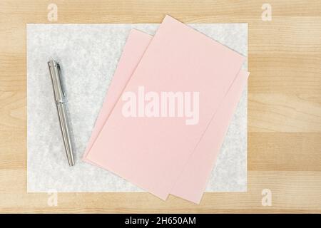 Rosa Grußkarte mit silbernem Stift auf dem Holztisch Stockfoto