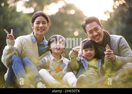 Glückliche asiatische Familie mit zwei Kindern, die im Stadtpark auf dem Rasen sitzen Stockfoto