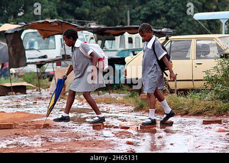 Junge Schülerinnen werden durch gebrochene Wasserpiopes in Harare über Wasserpfützen springen sehen. Harare's Wasserleitungen brechen und Tausende von Litern behandeltes Wasser gehen verloren. Simbabwe. Stockfoto