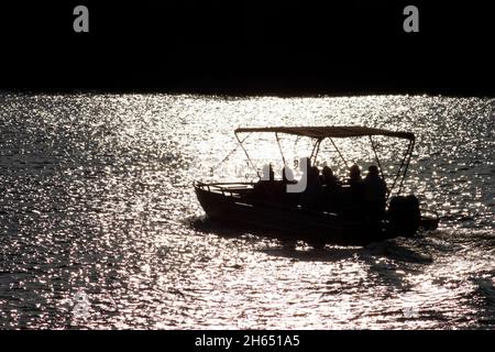 Ein Boot wird bei Sonnenuntergang auf dem Zambezi Fluss in Victoria Falls gesehen. Bootstouren bei Sonnenuntergang sind in den Victoria Falls beliebt, da die meisten Tiere wie das Nilpferd während des Sonnenuntergangs herauskommen. Simbabwe. Stockfoto