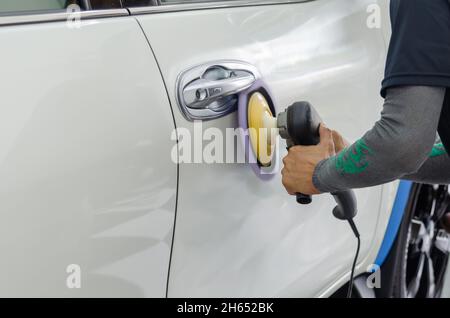 Mann bei der Arbeit Zum polieren, beschichten Autos. Polieren des Autos hilft Verunreinigungen auf der Oberfläche des Autos zu beseitigen. das Einwachsen der Auto Oberfläche c Stockfoto