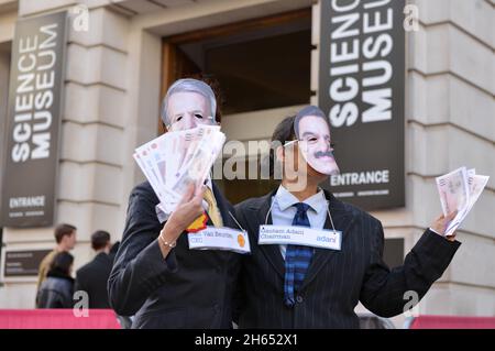 Demonstranten, die als Adani-Vorsitzender Gautam Adani und Shell-CEO Ben van Beurden gekleidet waren, posieren während der Demonstration mit gefälschtem Geld. Extinction Rebellion-Aktivisten veranstalteten einen Protest gegenüber dem Science Museum in South Kensington gegen das Sponsoring des Museums durch die fossilen Energiekonzerne Shell und Adani. Stockfoto