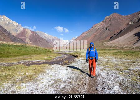 Ein Mann, der an einem kalten, sonnigen Tag entlang des gefrorenen Flusses im Aconcagua Provincial Park, Argentinien, vom Camp Comfluencia zum Basislager Plaza de Mulas wandert Stockfoto