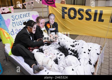 Aktivisten, die als Adani-Vorsitzender Gautam Adani, Science Museum Direktor Ian Blatchford und Shell-CEO Ben van Beurden gekleidet sind, liegen während der Demonstration auf einem Bett mit gefälschtem Geld, Kohle und gefälschtem Öl. Extinction Rebellion-Aktivisten veranstalteten einen Protest gegenüber dem Science Museum in South Kensington gegen das Sponsoring des Museums durch die fossilen Energiekonzerne Shell und Adani. Stockfoto