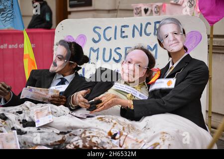 Aktivisten, die als Adani-Vorsitzender Gautam Adani, Science Museum Direktor Ian Blatchford und Shell-CEO Ben van Beurden gekleidet sind, liegen während der Demonstration auf einem Bett mit gefälschtem Geld, Kohle und gefälschtem Öl. Extinction Rebellion-Aktivisten veranstalteten einen Protest gegenüber dem Science Museum in South Kensington gegen das Sponsoring des Museums durch die fossilen Energiekonzerne Shell und Adani. Stockfoto