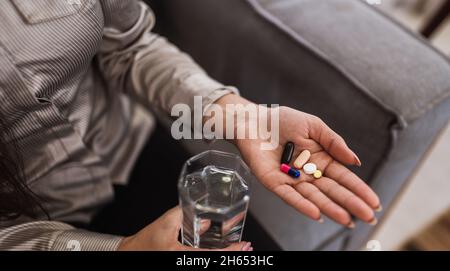 Nahaufnahme einer Frau, die verschiedene Tabletten, Pillen und ein Glas Wasser in der Hand hält. Einnahme von Vitaminen, Medikamenten und Nahrungsergänzungsmitteln. Das Konzept der Krankheit pre Stockfoto