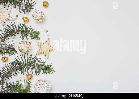 Komposition zu Weihnachten oder Neujahr. Bordüre aus Tannenzweigen und goldenen Verzierungen auf weißem Hintergrund. Flach liegend, Draufsicht, Kopierbereich. Stockfoto