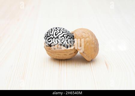 Walnussschale mit einer Miniatur-Stahlkopie eines menschlichen Gehirns auf einem Holztisch. Natürliche Supernahrung und psychische Gesundheit Konzept. Stockfoto