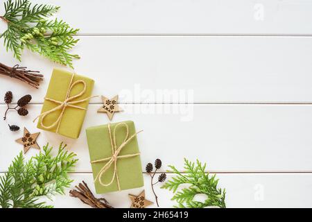 Weihnachts- oder Neujahrsarrangement. Eckrand aus Geschenkschachteln, Nadelholzzweigen und natürlichen Dekorationen auf weißem Holzhintergrund. Flach legen, bis Stockfoto