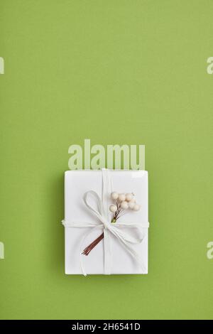 Eine Geschenkschachtel in weißem Papier verpackt und mit Band und Beeren auf grünem Hintergrund dekoriert. Draufsicht, flach liegend, Kopierbereich. Stockfoto