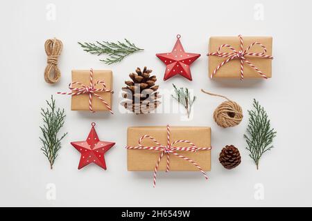 Weihnachtskomposition mit Geschenkschachteln, eingewickelt in Bastelpapier, Tannenzapfen, Nadelholzzweigen, dekorativen Spielzeugen auf weißem Hintergrund. Flach liegend, Draufsicht. Stockfoto