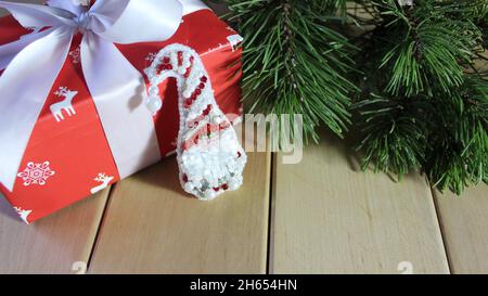 Weihnachtsknome mit einem Geschenk und einem grünen Tannenzweig. Die Geschenkbox ist festlich mit einem weißen Band verziert. Neujahr. Weihnachtssymbol. Stockfoto