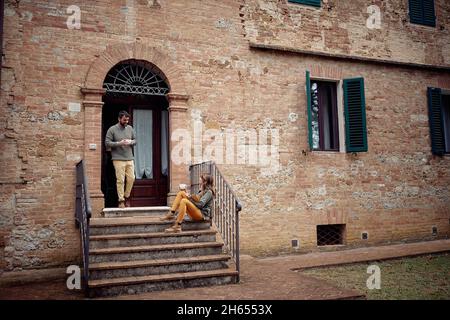 Ein junges Paar genießt Kaffee und ein Gespräch, während es eine Zeit auf der Treppe in entspannter Atmosphäre vor dem Haus verbringt. Stadt, außerhalb, Ruhe, Stockfoto