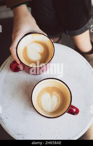 Zwei rote Tassen Kaffee auf dem Tisch und die Beine des Mädchens Stockfoto