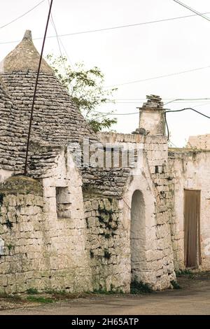 Gruppe von alten Trulli auf dem Land, traditionelle alte Haus und alte Steinmauer in Apulien, Italien, Europa, vertikal Stockfoto
