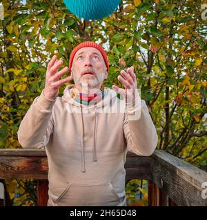 Ein älterer Mann (Ende der 60er Jahre) wirft einen schweren Slam Ball nach oben, ein Hinterhof-Workout am kalten Herbstnachmittag Stockfoto