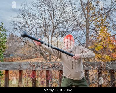 Älterer Mann (Ende der 60er Jahre) trainiert mit einer Stahlmace in seinem Hinterhof, Herbstlandschaft Stockfoto