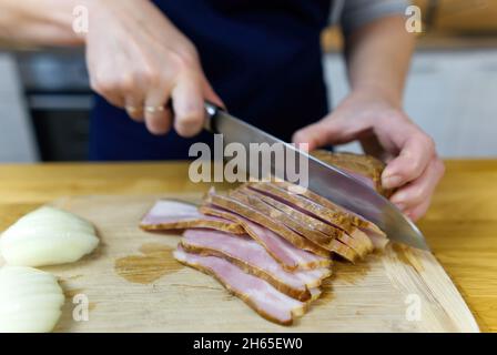 Cook schneidet Speck auf einem Holzbrett Stockfoto