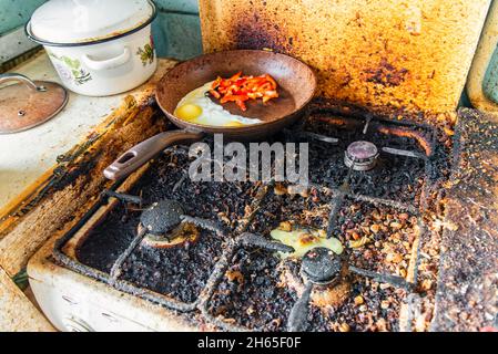 Dreckiger Herd und zerbrochenes Hühnereier, Pfanne mit Spiegelei und Paprika Stockfoto