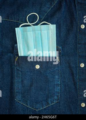 Pandemie-Konzept, schützende medizinische Einwegmaske in Denim-Hemdtasche Stockfoto