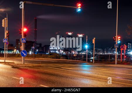 Helsinki / Finnland - 12. NOVEMBER 2021: Leere Stadtstraße mit Ampeln und beleuchteten Wolkenkratzern im Hintergrund. Stockfoto