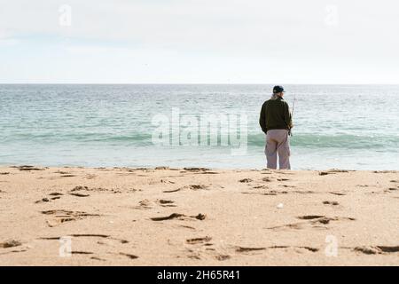 Einsamer älterer Mann, der am Strand angeln kann. Ältere Person genießt den Ruhestand durch das Meer Konzept Stockfoto