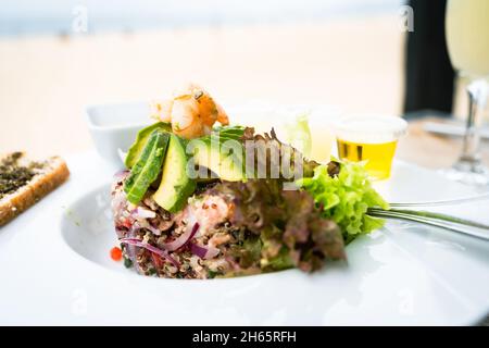 Ceviche-Teller mit frischen Meeresfrüchten und Quinoa und Salat auf der Seite. Gehackter Lachs, Garnelen und Avocado-Scheiben darauf. Gourmet Restaurant Food Konzept Stockfoto