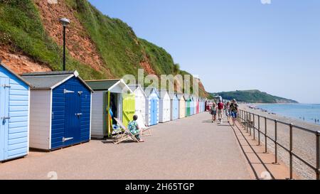 Seaton Devon Menschen, die sich an den Strandhütten entlang der Promenade am Seaton Devon England GB Europe sonnen Stockfoto