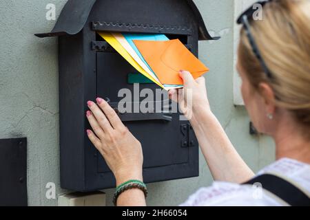 Der Postbetreiber fügt Briefe in das Postfach ein. Frau hält bunte Umschläge. Postarbeiter, der Korrespondenz liefert Stockfoto