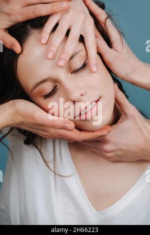Fröhliche Frau mit angenehmen Gesichtsmassage mit mehreren Kosmetikerinnen Hände berühren ihr Gesicht. Stockfoto
