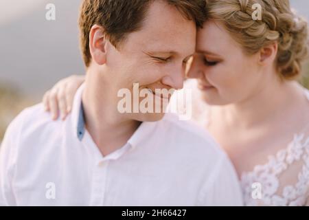 Lächelnde Braut umarmt sich hinter dem Bräutigam. Hochformat Stockfoto