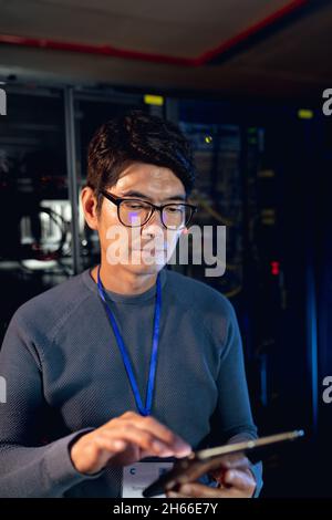 Männlicher Ingenieur aus Asien, der im Computerserverraum ein digitales Tablet verwendet Stockfoto