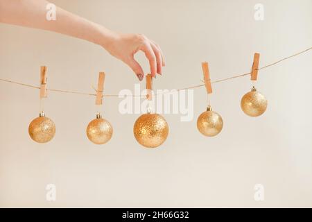 Goldene Deko-Kugeln von Hand am Seil festmachen. Weihnachtskugeln und Ornamentkugeln auf Weiß gesetzt Stockfoto