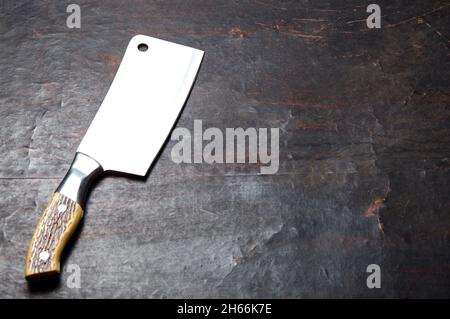 Fleischspalter auf dunklem Holzhintergrund. Küchenmesser oder Metzgerspalter aus Edelstahl auf einer Holzplatte Stockfoto