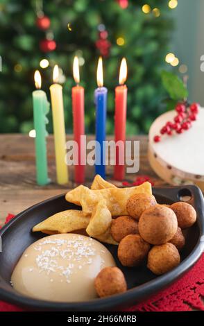 Tag Bei Kerzenschein. Typisch kolumbianisches Essen. Buñuelo, Pudding und Flocken mit Kerzen und Weihnachtsbaum im Hintergrund. Traditioneller kolumbianischer Urlaub. Stockfoto