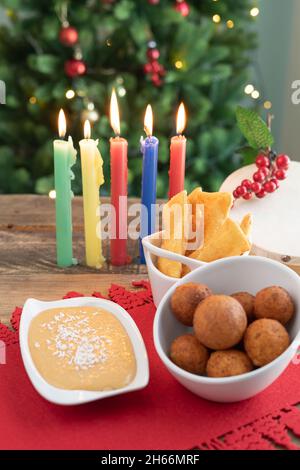 Tag Bei Kerzenschein. Typisch kolumbianisches Essen. Buñuelo, Pudding und Flocken mit Kerzen und Weihnachtsbaum im Hintergrund. Traditioneller kolumbianischer Urlaub. Stockfoto