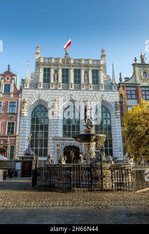 DANZIG, POLEN - 08. Okt 2021: Neptuns-Brunnen vor dem Artus-Hof-Gebäude mit Stadtflagge auf der Oberseite in Danzig, Polen Stockfoto