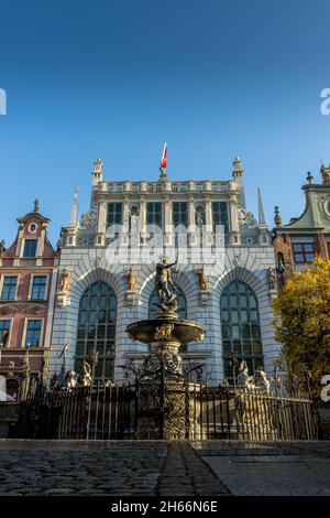 DANZIG, POLEN - 08. Okt 2021: Neptuns-Brunnen vor dem Artus-Hof-Gebäude mit Stadtflagge auf der Oberseite in Danzig, Polen Stockfoto
