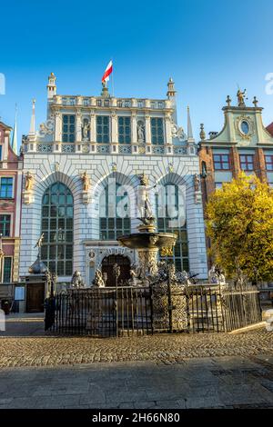 DANZIG, POLEN - 08. Okt 2021: Neptuns-Brunnen vor dem Artus-Hof-Gebäude mit Stadtflagge auf der Oberseite in Danzig, Polen Stockfoto