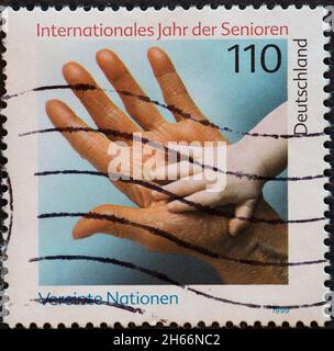 DEUTSCHLAND - UM 1999 : eine Briefmarke aus Deutschland, die eine Hand eines Kindes in der Hand eines älteren Kindes zeigt. Internationales Jahr der Senioren Stockfoto