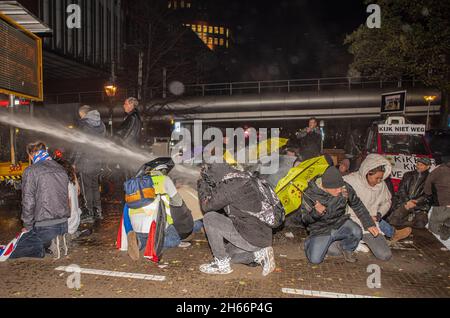 Polizeibeamte verwendeten Wasserwerfer, um Demonstranten während der Demonstration zu zerstreuen.Polizeibeamte von Riot sehen sich Demonstranten gegenüber, als sie sich während einer Pressekonferenz des niederländischen Premierministers Mark Rutte in Den Haag versammelten, um neue Covid-19-Beschränkungen bekannt zu geben. Stockfoto