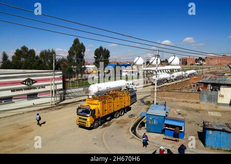 Senkata, El Alto, Bolivien. November 2021. Tankwagen für Flüssiggas und ein Lieferwagen für Inlandsflaschen (gelb) vor der Senkata-Brennstofffabrik auf der Av 6 de Marzo / Camino Oruro in El Alto. Yacimientos Petrolíferos Fiscales Bolivianos (YPFB, Boliviens staatliches Öl- und Gasunternehmen) verfügt hier über eine große Raffinerie- und Speicheranlage, Die La Paz, El Alto und die Umgebung mit Benzin, Diesel und flüssigem Erdgas (in Flaschen für den Hausgebrauch, aber auch für Fahrzeuge und andere Industrien) versorgt. Im Hintergrund sind einige der sphärischen Gasspeichertanks zu sehen. Stockfoto