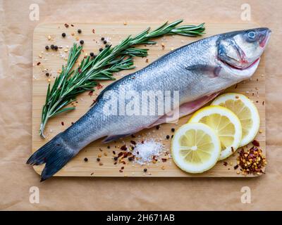 Rohe Zubereitung von ungekochten Meeresfischen - Seebarsch zur Auswahl von Fischen auf Schneidebrett auf dem Pergamentpapier. Mediterranes Meeresfrüchtekonzept. Draufsicht mit Kopie Stockfoto