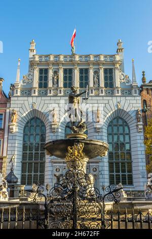 DANZIG, POLEN - 08. Okt 2021: Neptuns-Brunnen vor dem Artus-Hof-Gebäude mit Stadtflagge auf der Oberseite in Danzig, Polen Stockfoto